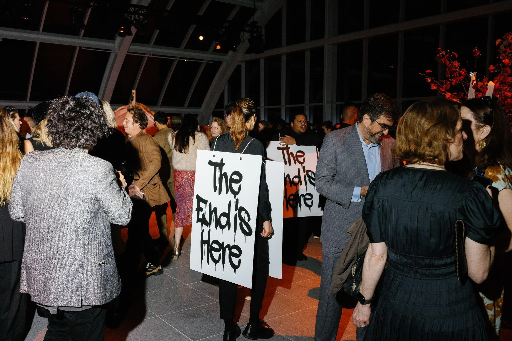 Performer at gala in the crowd of guests wearing a protest sign on their front and back reading the end is here