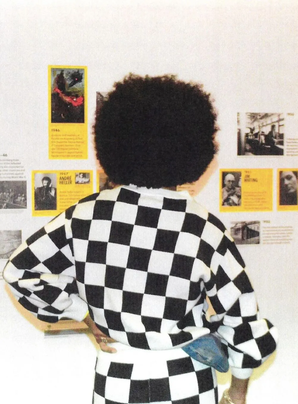 Woman in black and white checkered sweater views artist information panels on a white wall