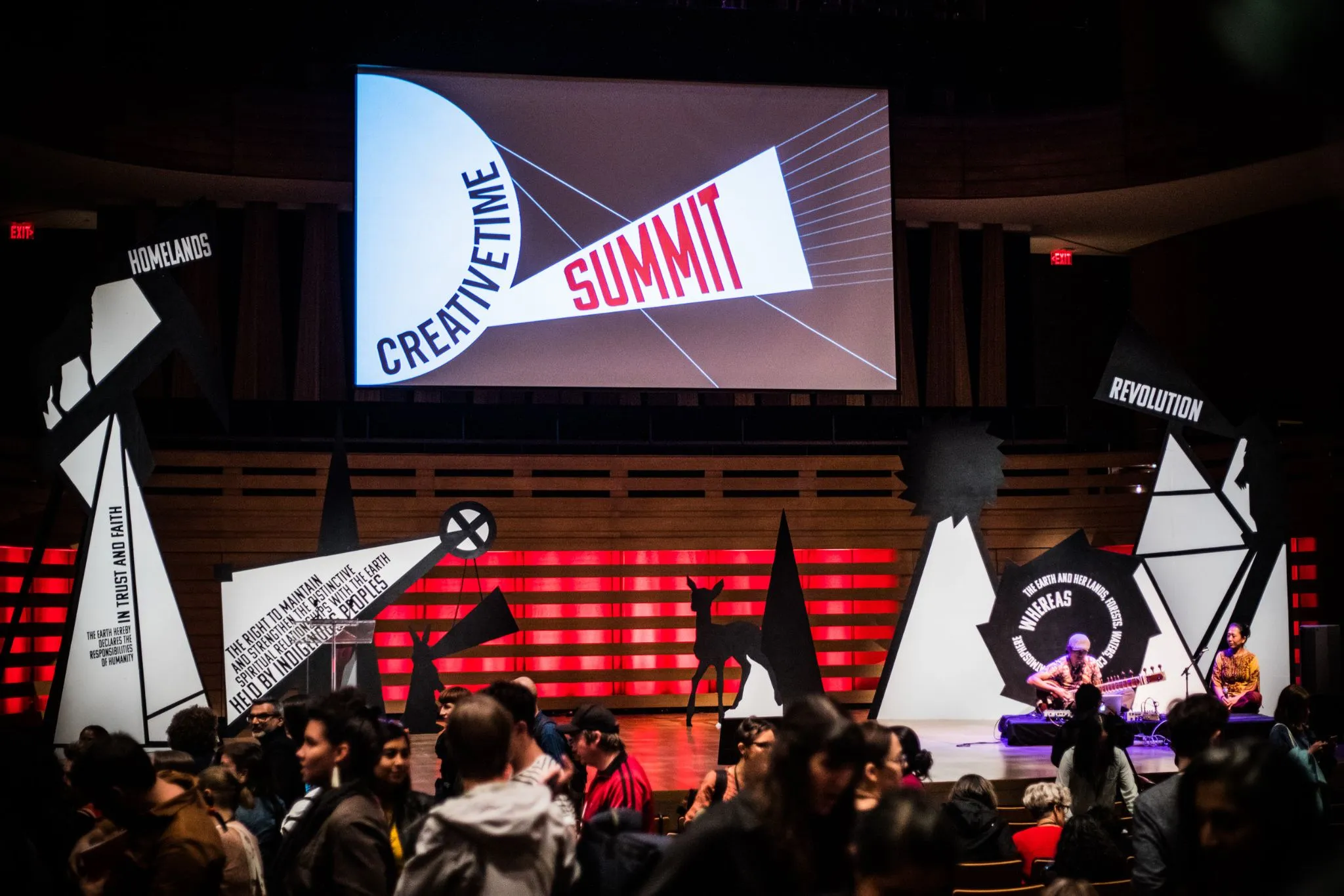 Decorated stage with musicians performing and event name on projection screen